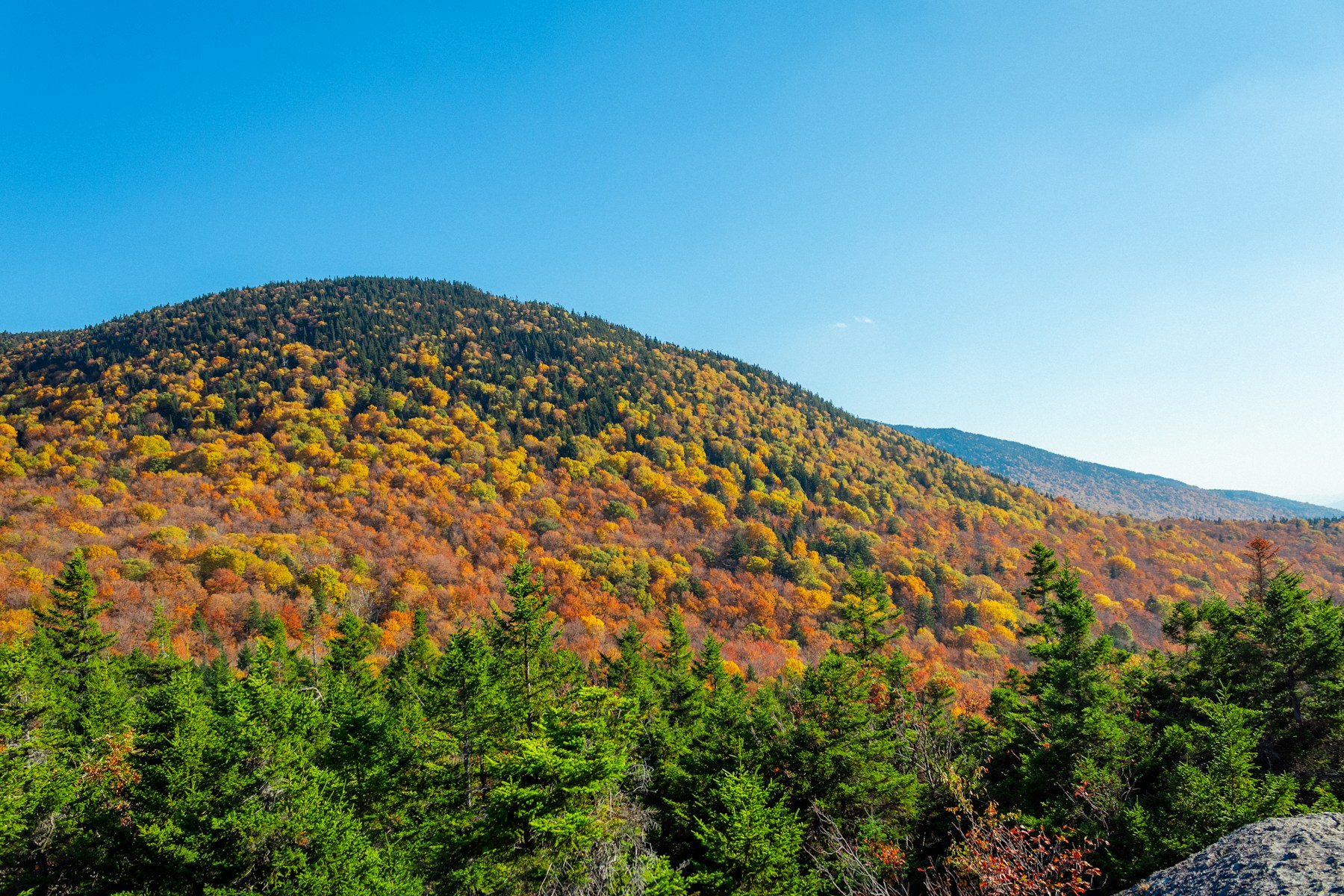 Autumn foliage covering the slopes of Stowe Pinnacle in Vermont under a clear sky
